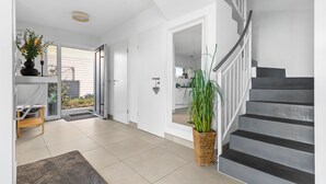 A modern interior with a staircase, a door leading to a kitchen, and a potted plant. - Maritimes & Sea – Vacation Home with Sauna and Ocean View on the Beach (Olpenitz)