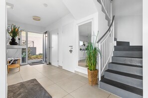 A modern interior with a staircase, a door leading to a kitchen, and a potted plant. - Maritimes & Sea – Vacation Home with Sauna and Ocean View on the Beach (Olpenitz)