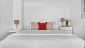A minimalist bedroom with a large bed, two bedside tables, and a nightstand with a lamp and a plant. - Maritimes & Sea – Vacation Home with Sauna and Ocean View on the Beach (Olpenitz)