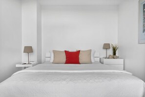 A minimalist bedroom with a large bed, two bedside tables, and a nightstand with a lamp and a plant. - Maritimes & Sea – Vacation Home with Sauna and Ocean View on the Beach (Olpenitz)