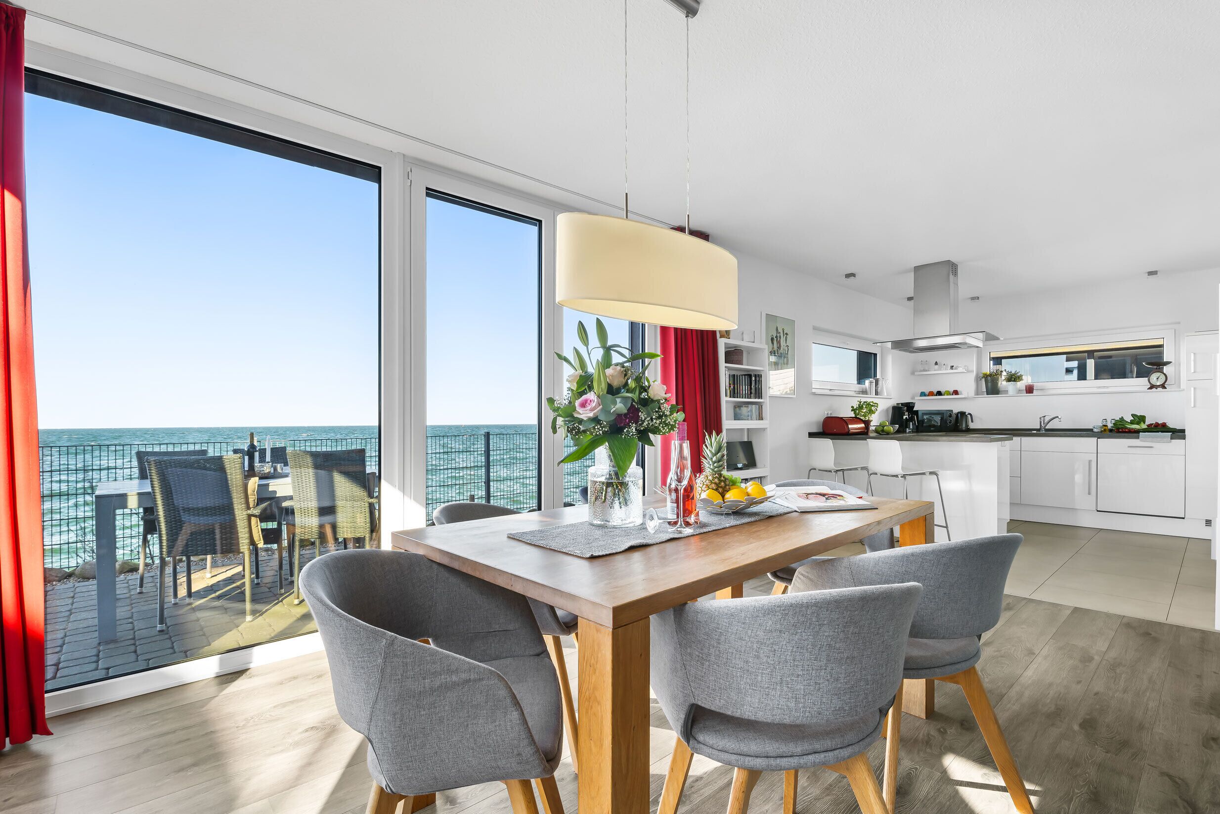 A modern kitchen with white cabinets, a stainless steel range hood, and a dining area with a wooden table and grey chairs.