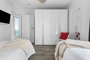Une chambre moderne avec deux lits, une armoire, un téléviseur et une vue sur la mer.