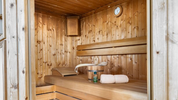 A sauna with wooden benches, a bench heater, a towel, and a bottle of sauna salt. - Maritimes & Sea – Vacation Home with Sauna and Ocean View on the Beach (Olpenitz)