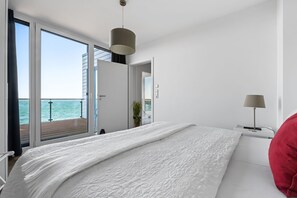 A bedroom with a large bed, a view of the sea through a sliding door, and a balcony. - Maritimes & Sea – Vacation Home with Sauna and Ocean View on the Beach (Olpenitz)