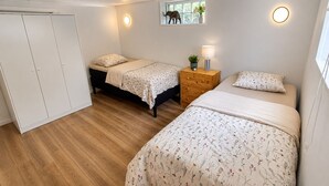 Um quarto com duas camas, um guarda-roupa, uma mesa de cabeceira com uma luminária e uma janela com vista para árvores.