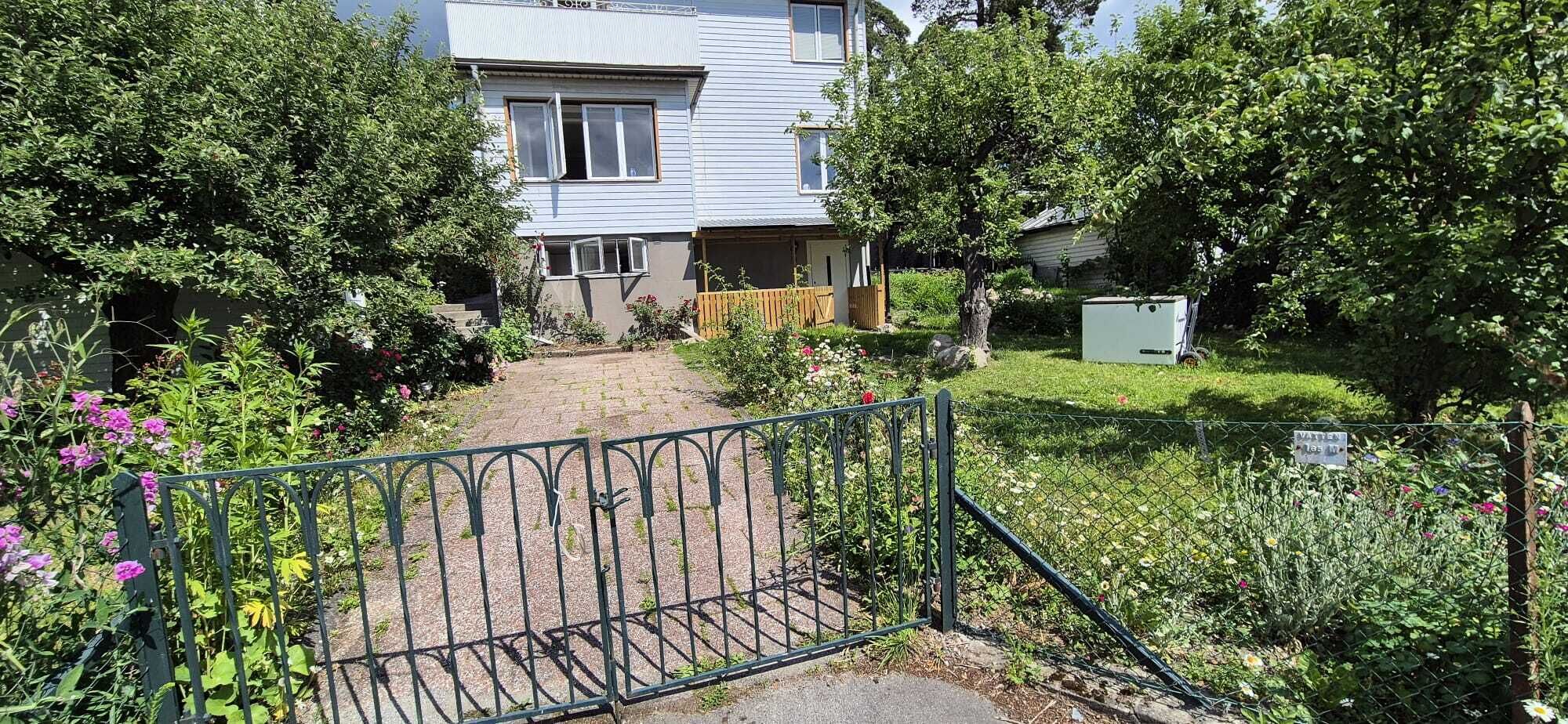 En bostadsfastighet med en asfalterad uppfart som leder fram till huset, omgiven av frodig grönska och ett staket av metall.