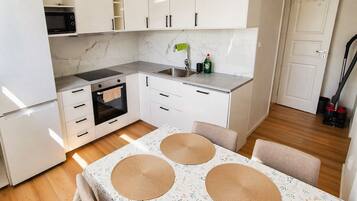 A compact kitchen with white cabinets, a microwave, an oven, and a sink. There is a table with a floral tablecloth and woven placemats.