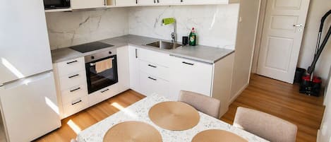 A compact kitchen with white cabinets, a microwave, an oven, and a sink. There is a table with a floral tablecloth and woven placemats.