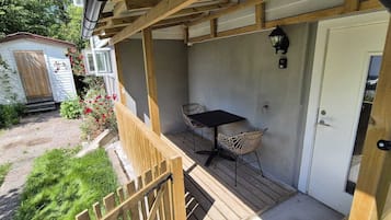 A covered outdoor seating area with a table and two chairs, a wooden deck, and a white door.