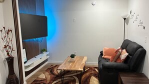 Un salon moderne avec un téléviseur à écran plat, un canapé en cuir noir, une table basse en bois et un tapis à motifs.