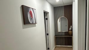Un couloir avec un plancher en bois, une porte, un miroir fixé au mur et un tableau encadré.