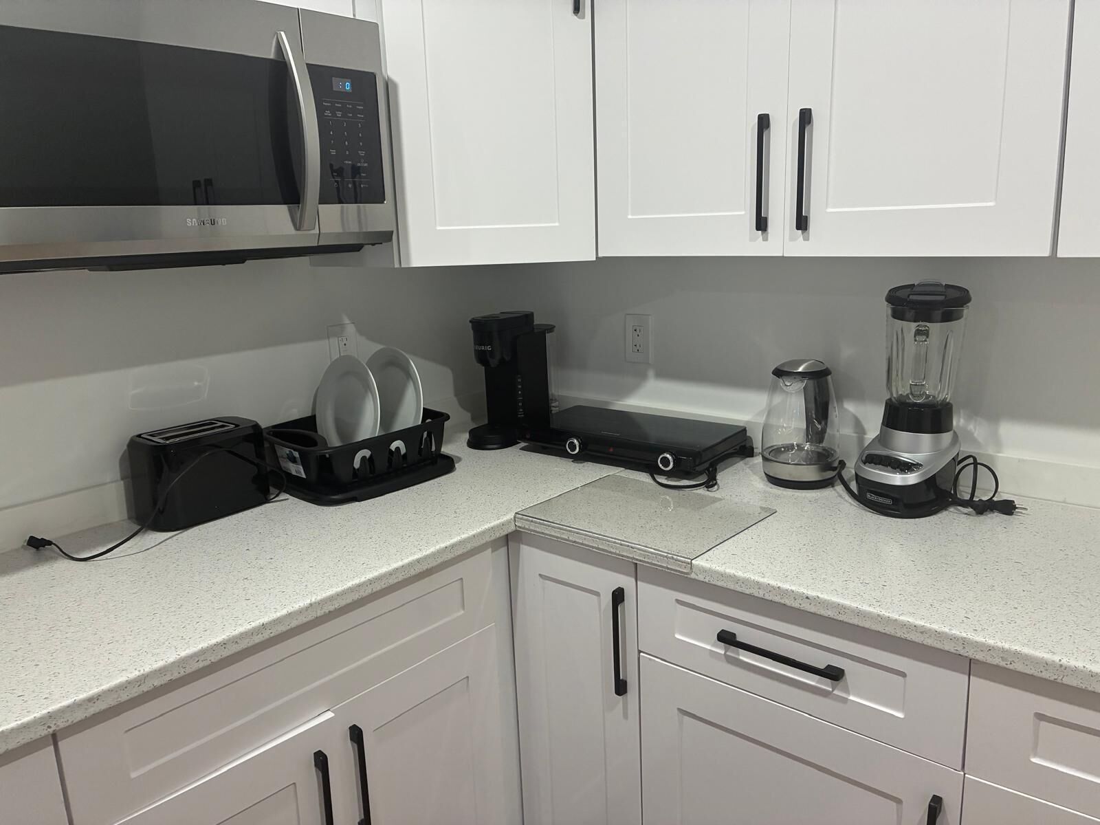 A kitchen with white cabinets, a microwave, a toaster, a coffee maker, and a blender.