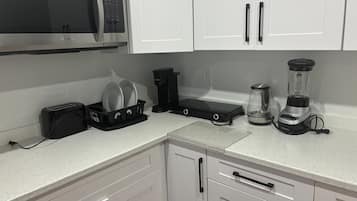 A kitchen with white cabinets, a microwave, a toaster, a coffee maker, and a blender.