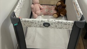 Un parc pour bébé doté d’un dessus en tissu à mailles, d’un fond rembourré et d’un panneau latéral orné d’un motif en forme d’étoile. À l’intérieur, on trouve deux peluches et un petit coussin avec un motif représentant un visage d’ours.