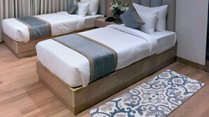 A hotel room with two beds, a ceiling fan, a nightstand with a phone, and a patterned rug. - Hotel Ramaya Luxury  (Jaipur)