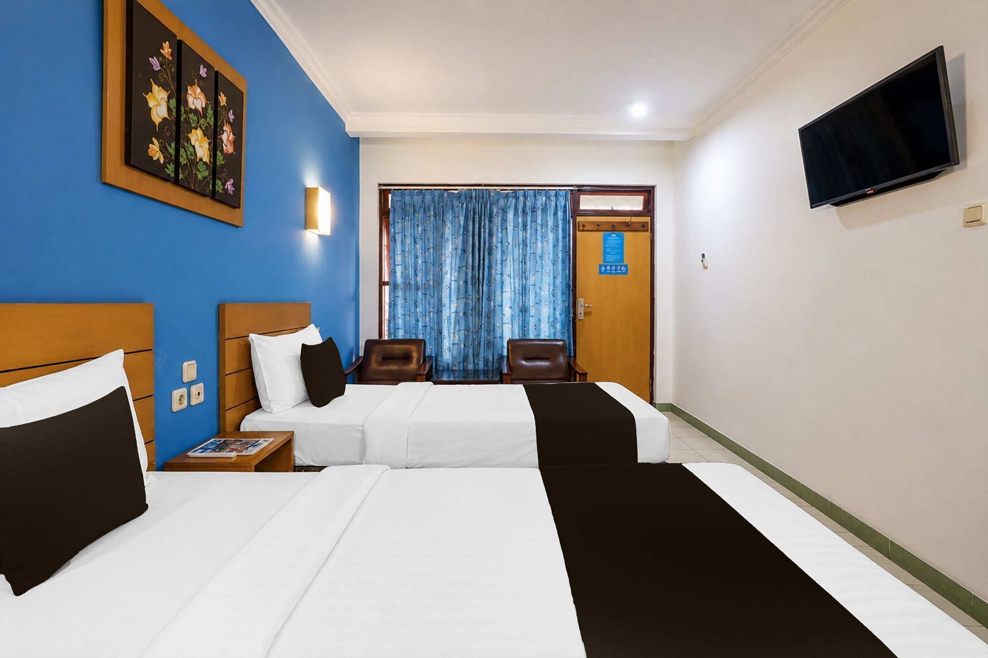 A hotel room with two beds, a television, a painting, and a window with curtains.
