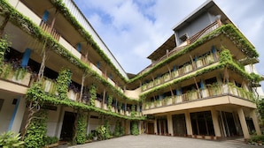 A multi-story building with balconies covered in greenery, a paved courtyard, and a clear sky. - Townhouse Oak Hotel Lestari (Kaliwates)