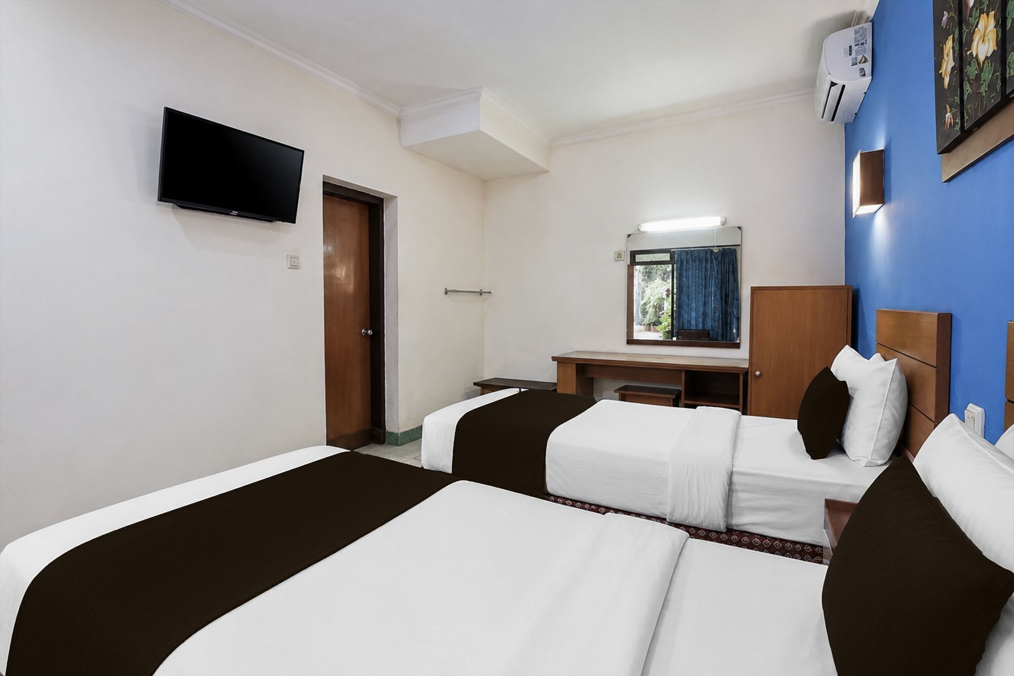 Habitación de hotel con dos camas, un escritorio, un espejo y una televisión.