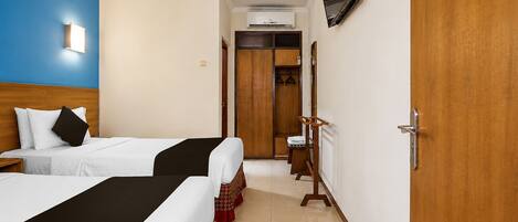 A hotel room with two beds, a wardrobe, a television, and an air conditioning unit.