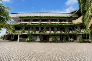 Un edificio de varios pisos con techo plano, rodeado por un patio empedrado.
