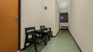 A narrow hallway with a wooden door on the left, a bench, and a table with chairs. - Townhouse Oak Hotel Lestari (Kaliwates)