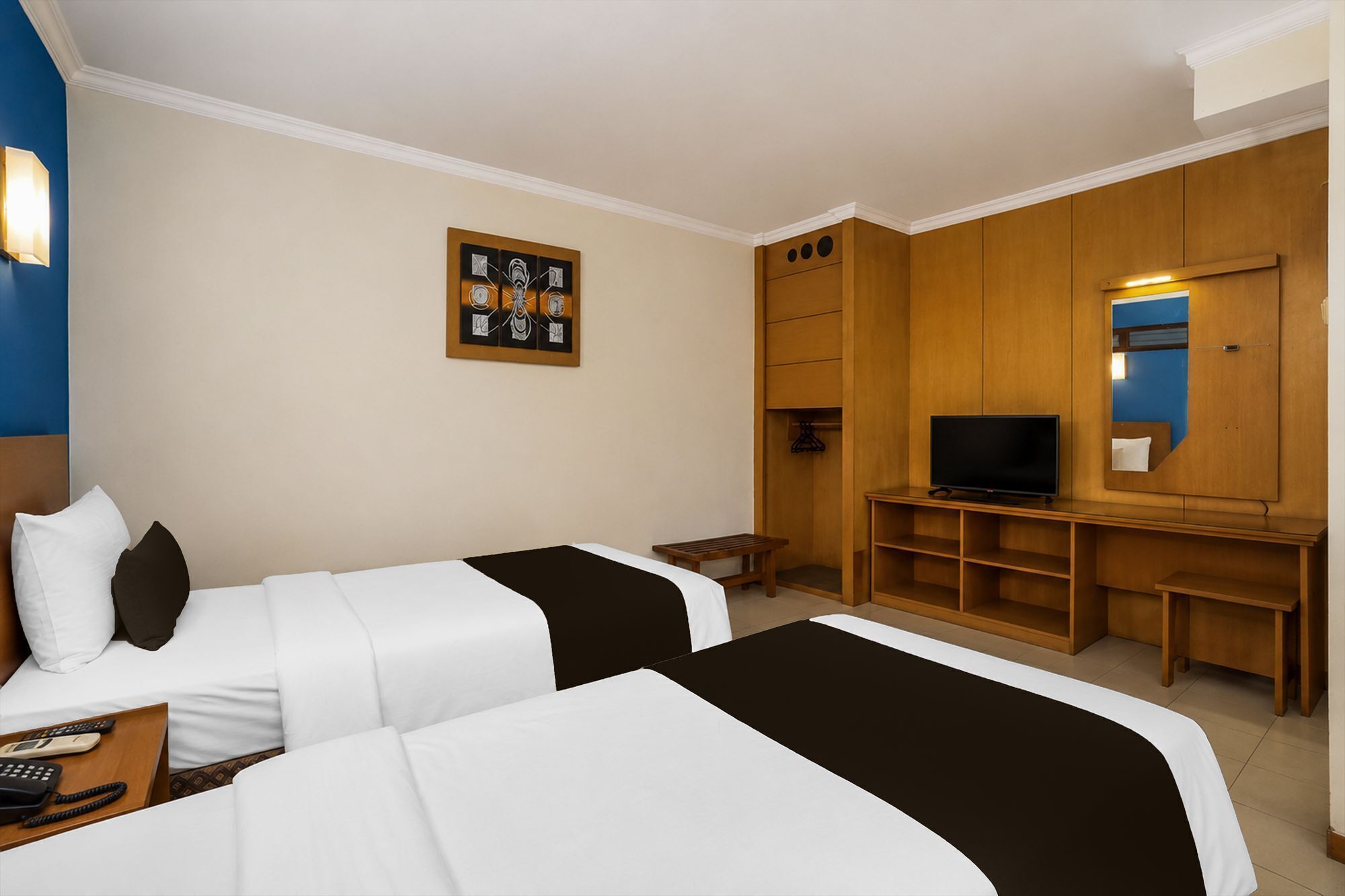 A hotel room with two beds, a television, a wooden desk, and a painting on the wall.