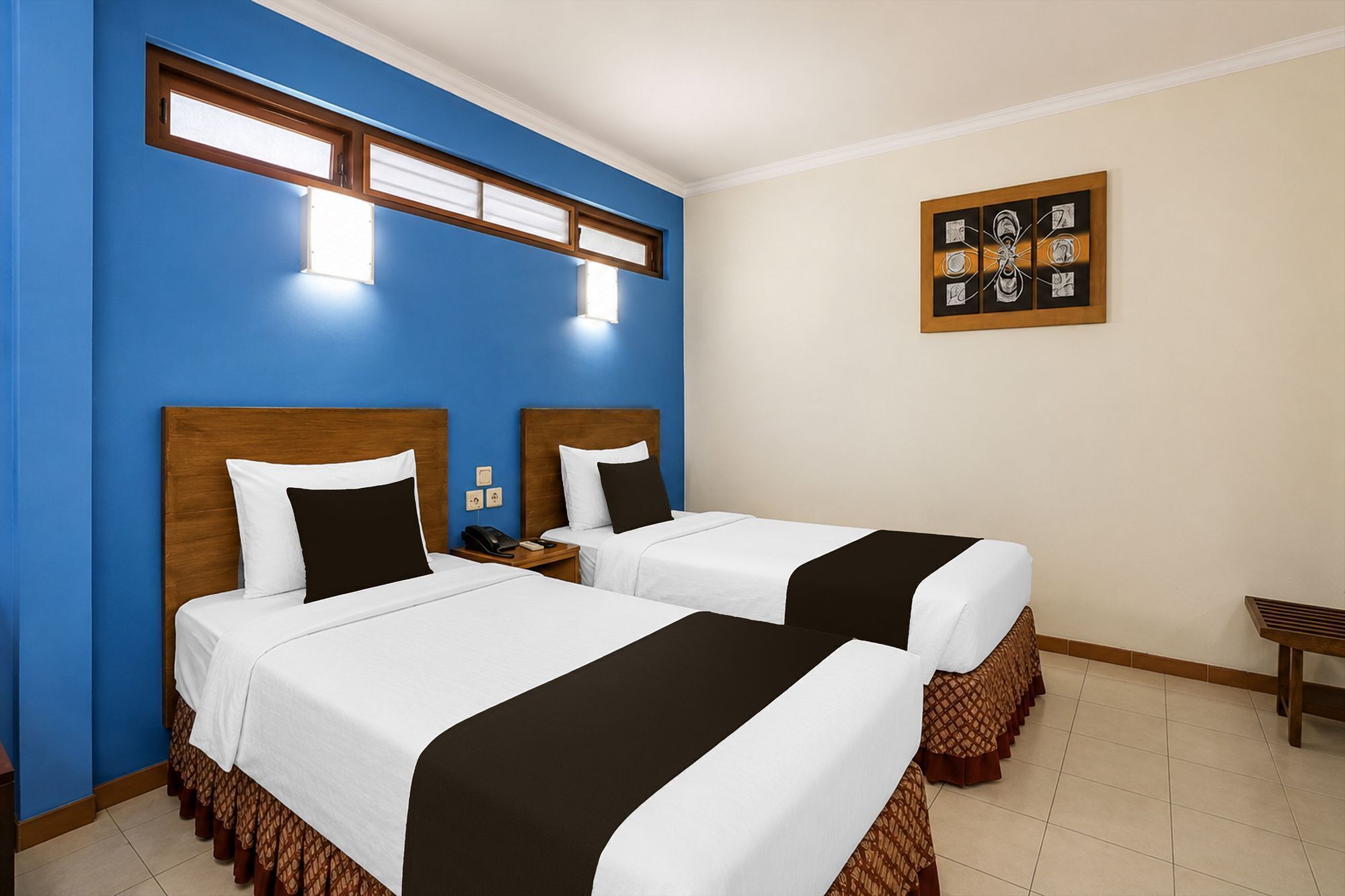 Habitación de hotel con dos camas, una mesita, una banca, una obra de arte en la pared y una ventana con persianas.