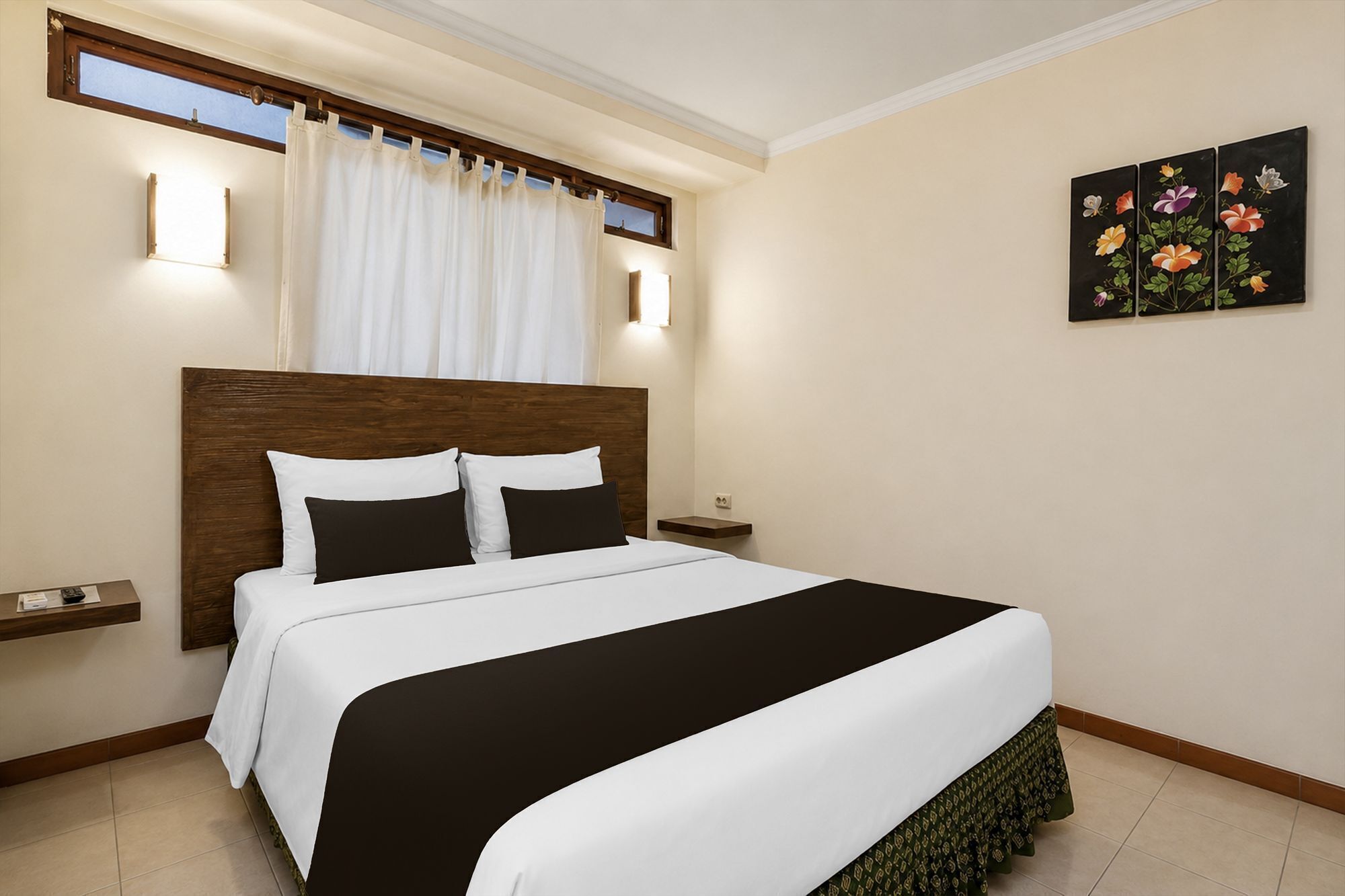 A hotel room with a bed, a nightstand, a wall-mounted light, a window with curtains, and a floral painting.