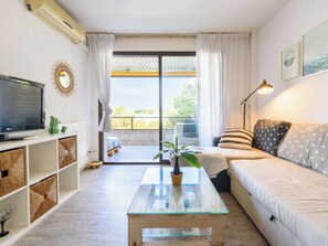 A modern living room with a sofa, a glass coffee table, a television, and a balcony with a view. - Apartment Uolas by Interhome (Salou)