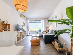 A modern living room with a sofa, ottoman, TV, and a large window with curtains. - Apartment Uolas by Interhome (Salou)