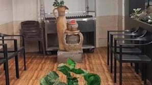 Interior de restaurante con una mesa central, sillas, un jarrón decorativo y una planta.
