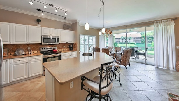 A spacious kitchen with a central island, modern appliances, and a dining area with wicker chairs. - First Floor With a View of the Lake (Naples)