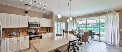 A spacious kitchen with a central island, modern appliances, and a dining area with wicker chairs.