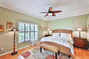 A bedroom with a bed, a ceiling fan, a window with blinds, a nightstand with a lamp, and a bench. - First Floor With a View of the Lake (Naples)