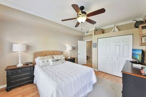 Ein Schlafzimmer mit Bett, Nachttischen, Schreibtisch, Deckenventilator und einer Tür zu einem anderen Raum.