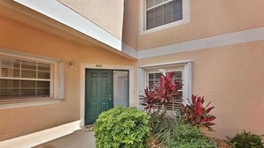 A residential building with a green door, a window with blinds, and a small garden with various plants. - First Floor With a View of the Lake (Naples)