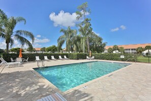 A swimming pool with lounge chairs and umbrellas, surrounded by palm trees and a hedge. - First Floor With a View of the Lake (Naples)