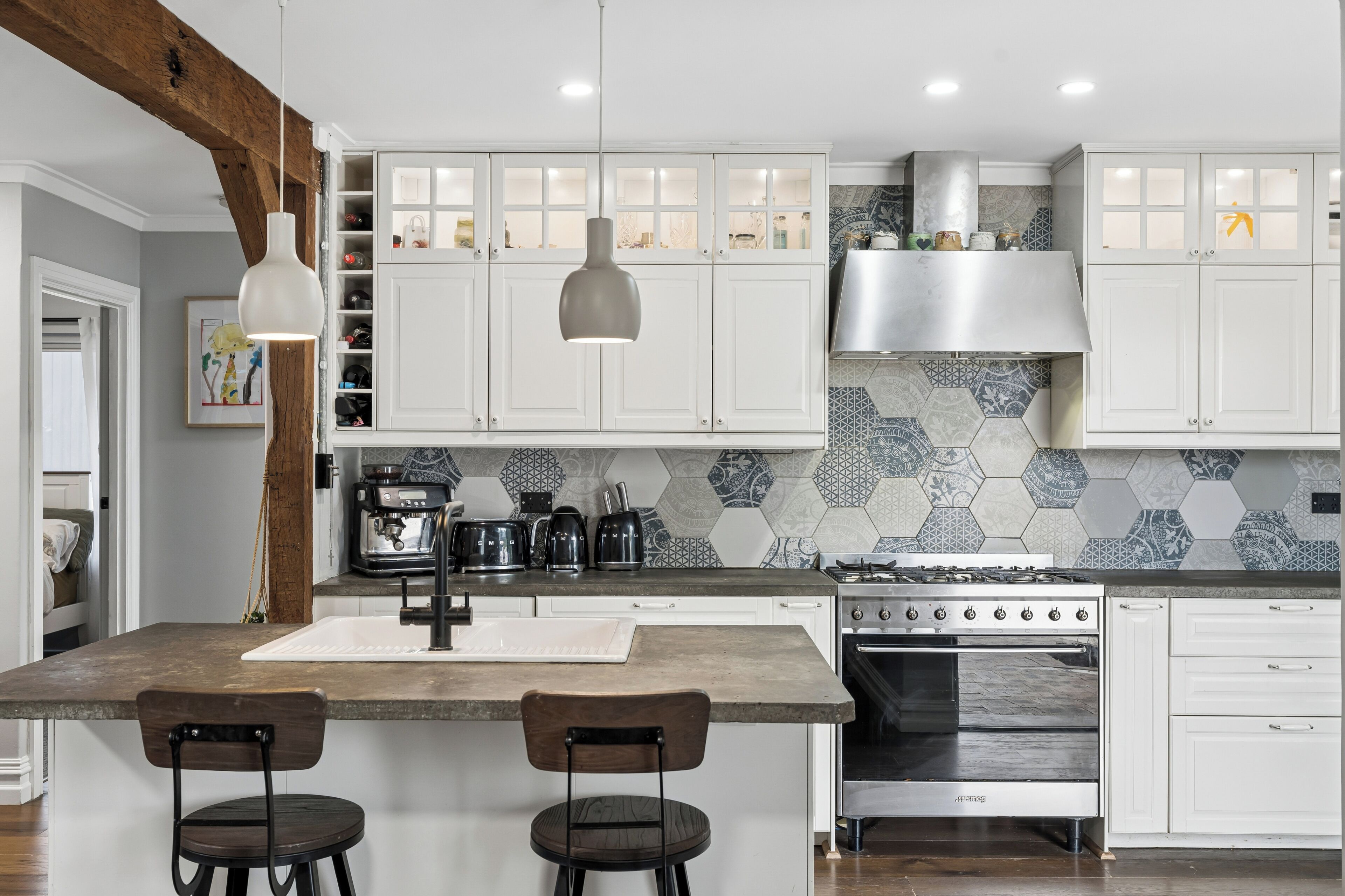 A modern kitchen with white cabinetry, a central island with bar stools, a stove, and a coffee machine.