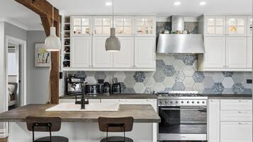 A modern kitchen with white cabinetry, a central island with bar stools, a stove, and a coffee machine.