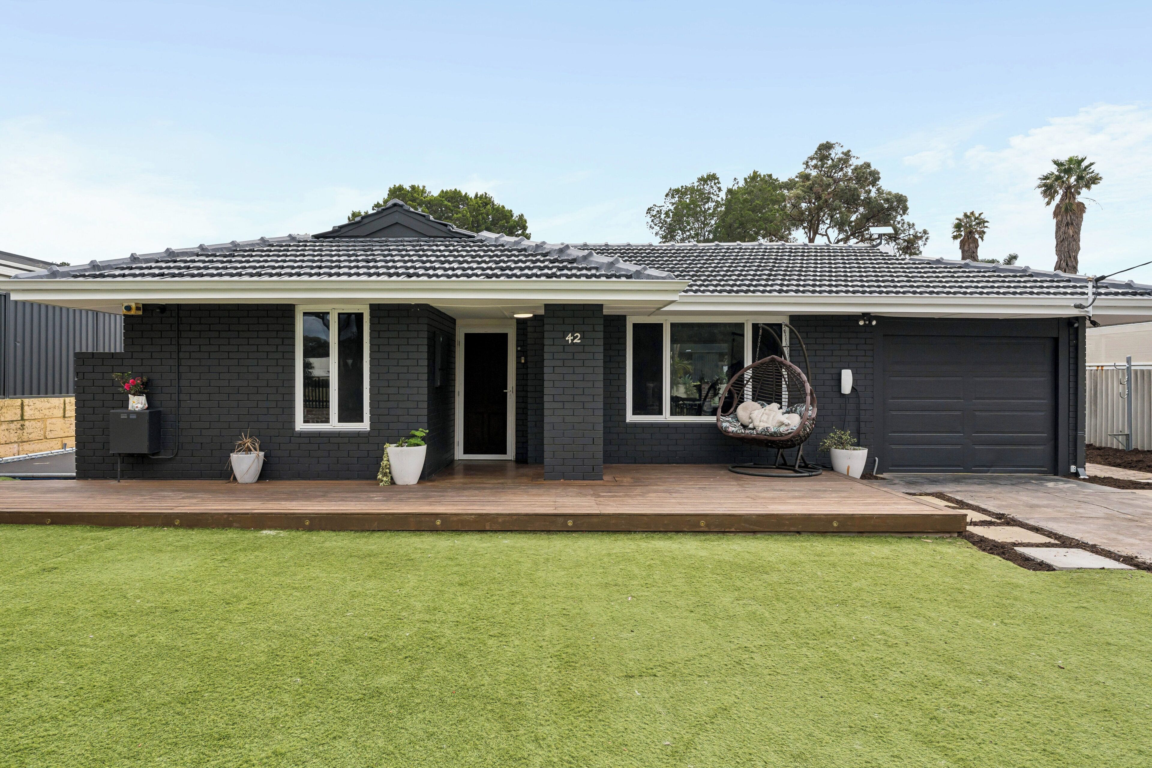 A modern two-story house with a dark exterior, a covered porch, and a front yard with grass and potted plants.
