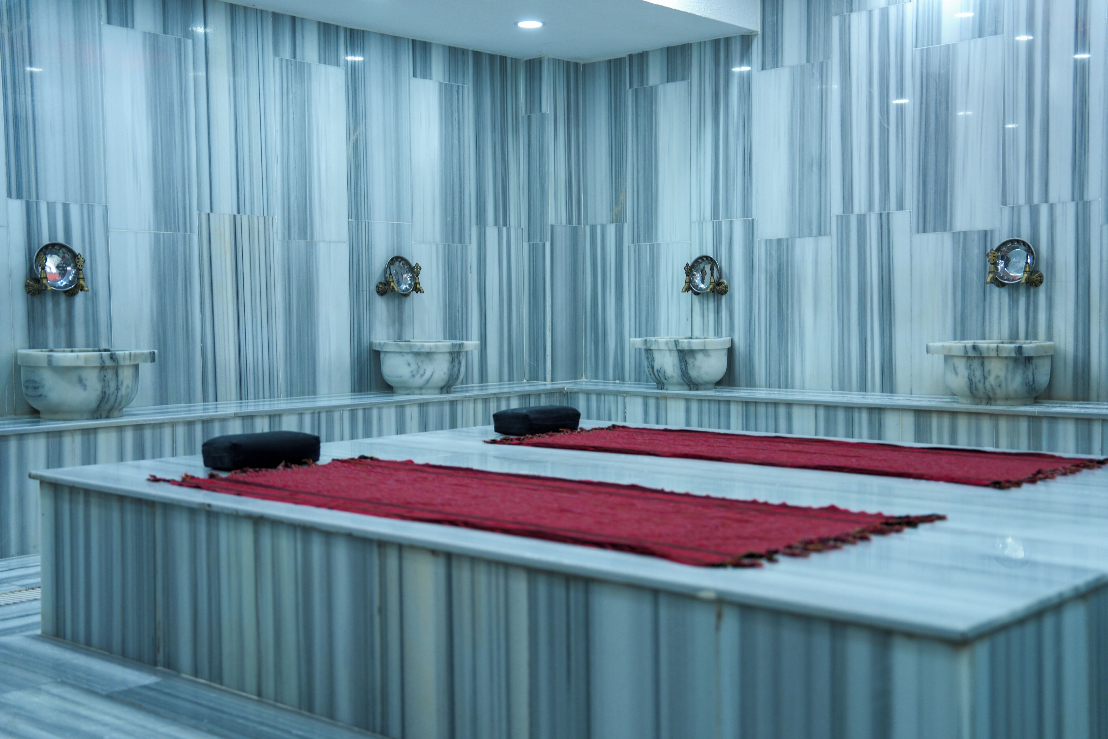 A bathroom with marble walls, multiple sinks, and red towels.