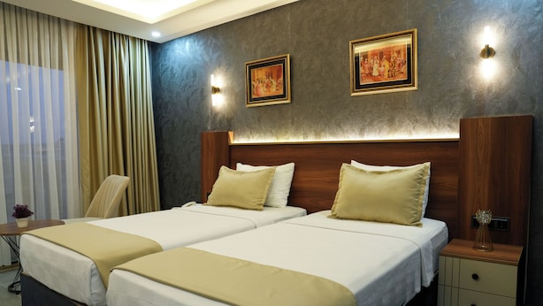 Habitación de hotel con dos camas, cabecera de madera, mesita de noche y lámpara de pared.