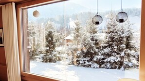 A room with a large window, wooden beams, a hanging light fixture, and a small table with a lamp. - An authentic chalet atmosphere with mountain views (Flühli)