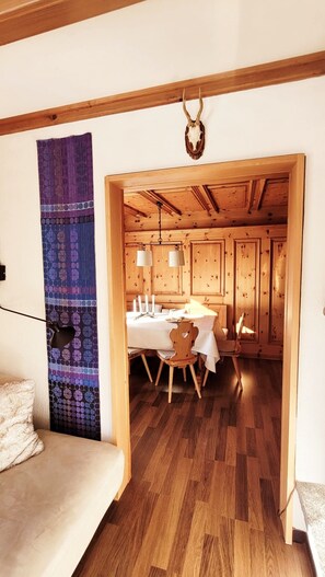 A wooden interior with a dining area, a hanging skull decoration, and a patterned tapestry.