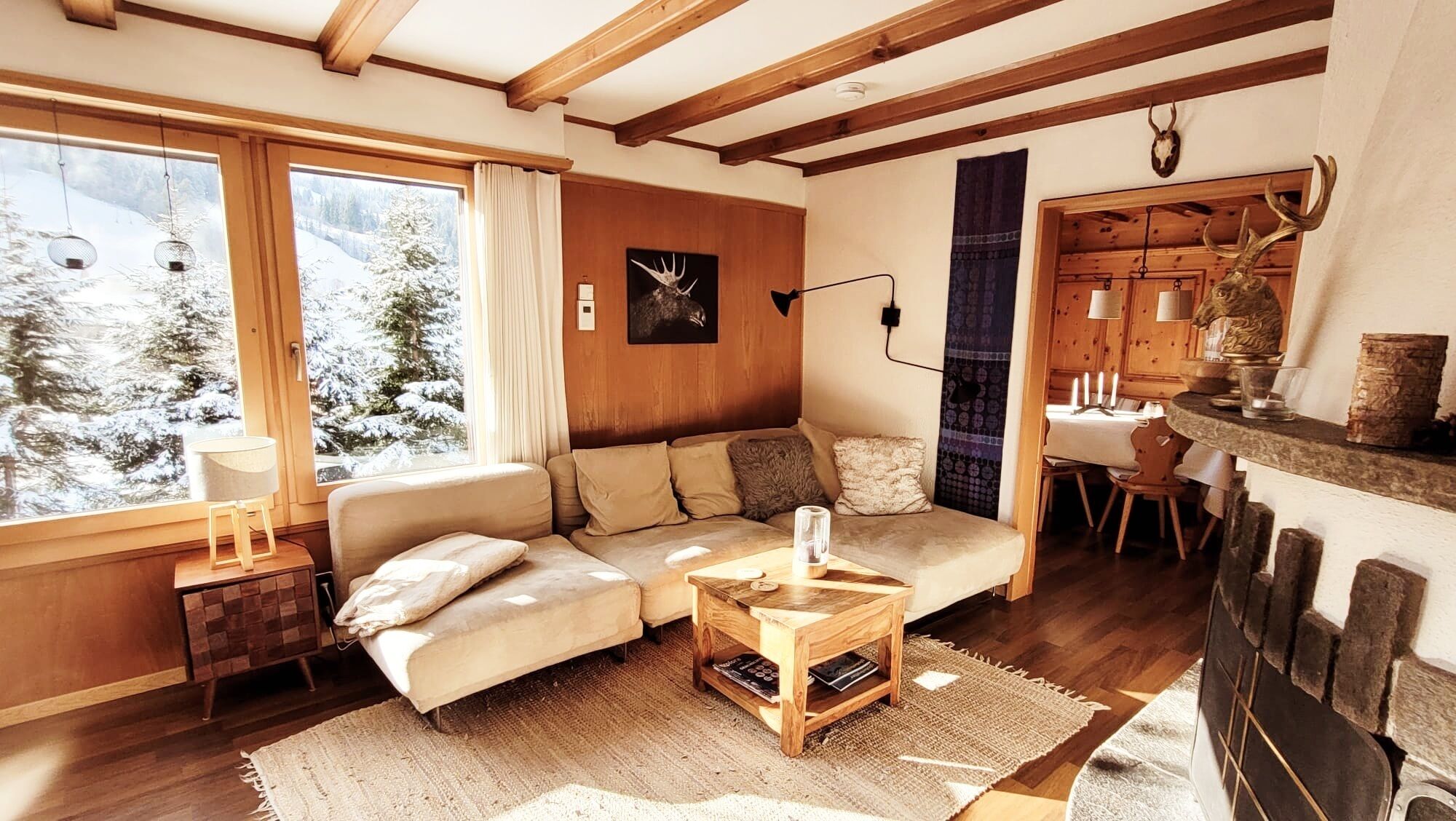 Ein gemütliches Wohnzimmer mit Holzbalkendecke, einer Sofagarnitur, einem Couchtisch und einem Kamin.