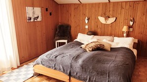 A bedroom with a wooden ceiling, a bed with a grey blanket, a cowhide rug, and a wall-mounted lamp. - An authentic chalet atmosphere with mountain views (Flühli)