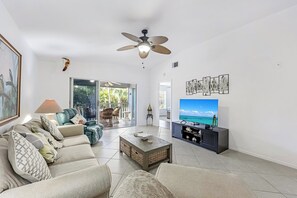 A living room with a sofa, coffee table, TV, and artwork on the wall. - Walk to the Beach from Vanderbilt Villas (Naples)