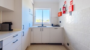 A compact kitchen with white cabinets, a window, and emergency equipment on the wall. - Jardins do Golfe Top Floor Retreat (Loulé)