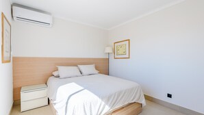 A bedroom with a bed, bedside tables, an air conditioning unit, a lamp, and a framed picture on the wall. - Jardins do Golfe Top Floor Retreat (Loulé)