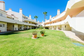 Un patio con un sendero central, rodeado de edificios blancos con varios balcones y dos palmeras.